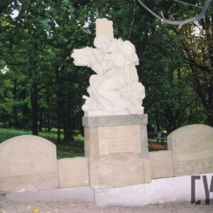 Szeroka płyta nagrobna, pośrodku postument z rzeźbą mężczyzny obejmującego krzyż, po bokach płyty nagrobne z inskrypcjami.