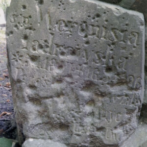 Uszkodzona kamienna tablica z napisami. Liczne ślady po pociskach.