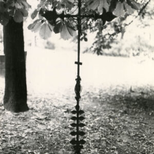 Żelazny krzyż łaciński z ramionami zdobionymi liliami andegaweńskimi. Na nim cynowa figurka Chrystusa. Krzyż otaczają gałęzie drzew.