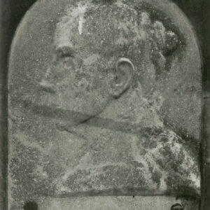 Kamienna plakieta w kształcie kwadratu zakończonego łukiem. Przedstawia popiersie kobiety w lewym profilu.