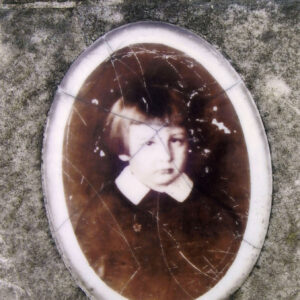 Owalny medalion ze zdjęciem chłopca z prostymi włosami i grzywką w kolorze sepii. 