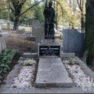 Duży, obmurowany nagrobek z kamienną płytą pośrodku. Po bokach wysypane białe kamyki. Na postumencie z czarną tablicą epitafijną stoi figura świętego Floriana. Z tyłu inne nagrobki i drzewa.