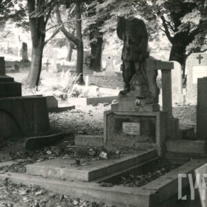 Obmurowana mogiła z płytą kamienną po środku. Na cokole duża rzeźba świętego Floriana pozbawiona głowy. Wokół inne nagrobki i drzewa.