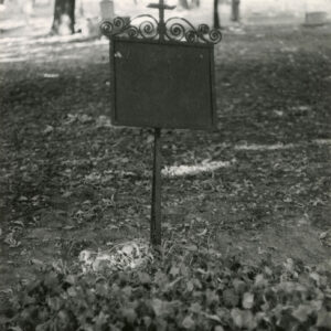 Prostokątna tablica, zwieńczona ażurową dekoracją, osadzona na wysokim pręcie, zakończonym krzyżem.