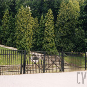 Dwuskrzydłowa, metalowa brama i fragment ogrodzenia, za którym znajdują się krzewy iglaste, schody i alejka.