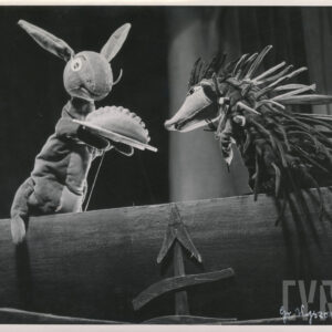 naprzeciw siebie znajdują się dwie kukiełki przedstawiające zająca i jeża, zając trzyma tackę z daniem przypominającym pieróg