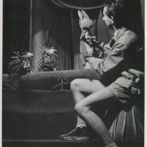 na scenie przysiadł mężczyzna ubrany w szorty, w rękach trzyma kukiełkę przedstawiającą zająca, obok znajdują się dwie kukiełki przedstawiające jeże