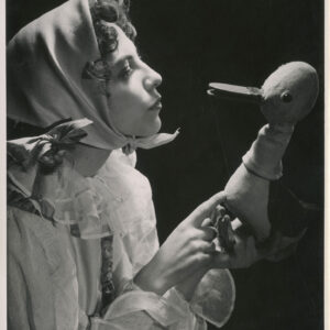 aktorka w białej sukni i chuście na głowie trzyma w rękach kukiełkę przedstawiającą Gęgorka