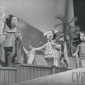 scena przy drewnianym płotku, trzy lalki ubrane w stroje z szerokimi rękawami stoją obok siebie w różnych pozach, we włosy mają wpięte kwiaty