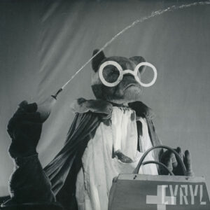 lalka przedstawiająca niedźwiedzia w białym fartuchu i długiej pelerynie z torbą lekarską, trzyma w ręce gruszkę medyczną, z której tryska woda