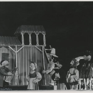 na scenie znajduje się sześć lalek w różnych pozach, za nimi fragment scenografii przedstawiającej budynek