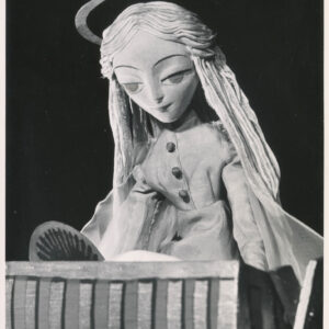 lalka z długimi włosami i aureolą, ubrana w długą suknię, pochyla się nad kołyską 