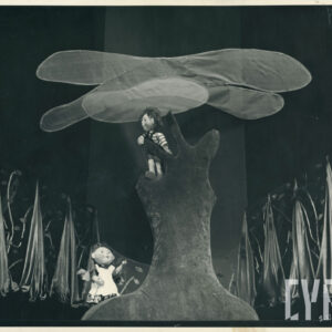 scena w lesie, na drzewie znajduje się lalka w krótkich spodniach na szelkach i koszulce w paski, pod drzewem druga lalka z długimi warkoczami w sukience i fartuszku