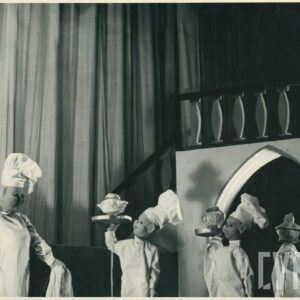 na scenie obok siebie stoją cztery lalki w fartuchach i czapkach kucharskich, trzy z nich trzymają wysoko na tacach naczynia o różnych kształtach