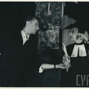 mężczyzna ubrany w togę i biret w lewej ręce trzyma księgę a w prawej białe pióro, obok niego stoi drugi mężczyzna ubrany w marynarkę z podwiniętymi rękawami, za nimi stoi duży zegar  