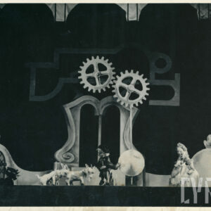 dekoracja przedstawiająca mechanizm zegara, dwa koła zębate i wahadło, na scenie znajduje się pięć lalek w tym dwa koziołki i czarny kot