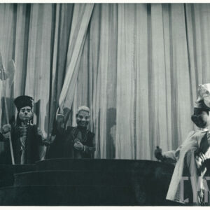 opuszczona kotara, na scenie znajdują się trzy lalki, pierwsza nosi na szyi szeroki łańcuch, druga ubrana w długą kamizelkę i czapkę trzyma w prawej ręce halabardę, trzecia ubrana w długi biały fartuch i kucharską czapkę