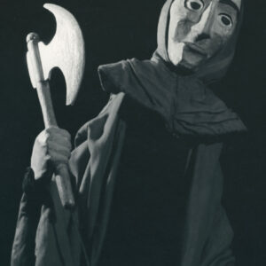 lalka ubrana w długą pelerynę i kaptur, w prawej ręce trzyma topór