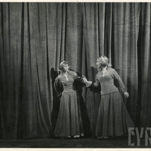 opuszczona kurtyna, przed nią stoją dwie kobiety w długich sukniach i opaskach na głowach