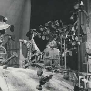 scena w sadzie, na scenie lalki, pośrodku stoi strach na wróble i mężczyzna w połatanym ubraniu, z lewej strony stoi starszy mężczyzna w kapeluszu z konewką w ręku, z prawej strony znajduje się studnia, z przodu rosną warzywa, z tyłu grusza i jabłonie