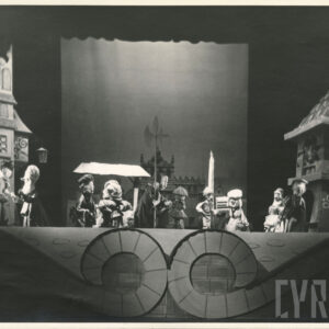 na scenie, pomiędzy kamienicą a wieżą, stoją parami lalki w różnych pozach, lalka mężczyzny stojąca pośrodku trzyma w ręce halabardę, przy wieży stoi pochylona lalka w pelerynie