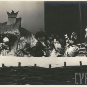 na scenie, przed domkiem pokrytym strzechą znajduje się sześć lalek w różnych pozach, jedna z nich leży z wyciągniętymi ku górze rękoma