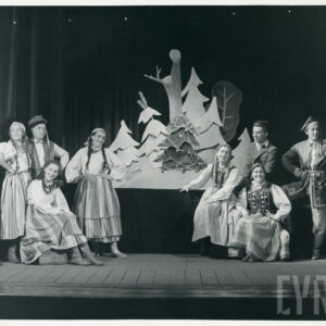 na scenie stoją i siedzą aktorzy w strojach regionalnych, za nimi udekorowana choinka i inne drzewa z kartonu