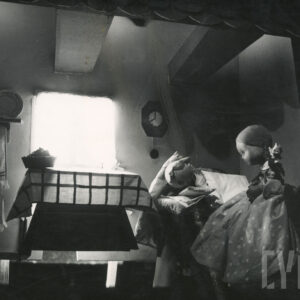 scenografia przedstawia wnętrze pokoju, na łóżku pod pościelą leży lalka, obok siedzi druga lalka w długiej sukience w kropki