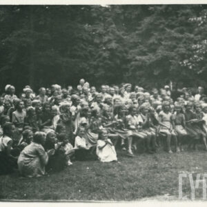 teren porośnięty trawą i drzewami, na którym stoją i siedzą ludzie w letnich ubraniach