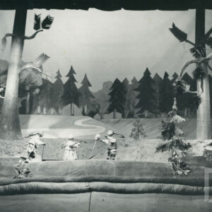 scena w lesie, trzy lalki przedstawiające zające stoją w kręgu, po prawej stronie świerszcz trzymający skrzypce w rękach, z tyłu ścieżka i drzewa