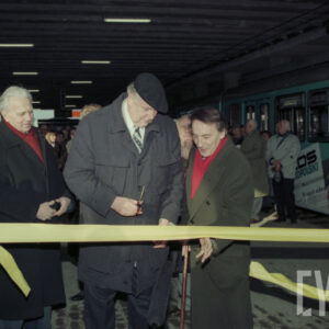 grupa osób stojąca na przystanku tramwajowym przy symbolicznej wstędze, którą jeden z mężczyzn przecina nożyczkami; w głębi stoi duża grupa osób przy tramwaju