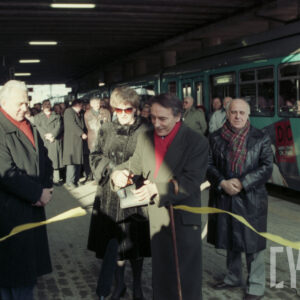 grupa osób stojąca na przystanku tramwajowym przy symbolicznej wstędze, którą jeden z mężczyzn przecina nożyczkami; w głębi stoi duża grupa osób przy tramwaju