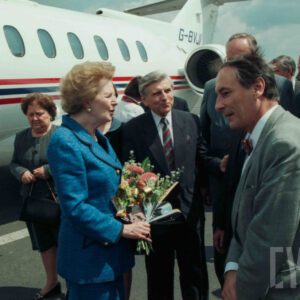 starsza, elegancka kobieta z kwiatami w dłoniach, rozmawiająca ze starszym mężczyzną ubranym w garnitur