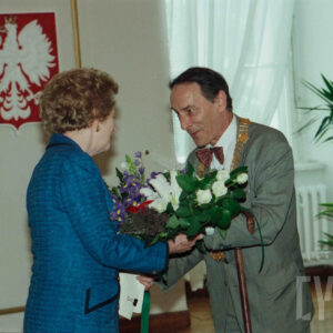 starsza kobieta i starszy mężczyzna w eleganckich ubraniach, mężczyzna wręcza kobiecie bukiet kwiatów