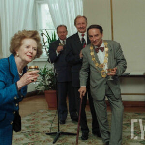 grupa odświętnie ubranych osób trzymająca w rękach kieliszki z winem