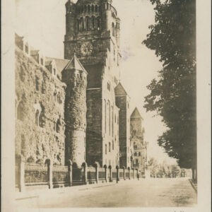 mury zamkowe pokryte dzikim winem, wysoka wieża zegarowa, u dołu wzdłuż ulicy kute ogrodzenie zamku, po prawej drzewa