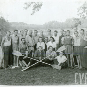 liczna grupa mężczyzn i dwie kobiety pozujący do fotografii w otoczeniu drzew i zieleni, dwóch mężczyzn trzyma wiosła