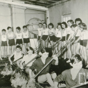 dzieci ubrane w stroje sportowe, trenujący w prowizorycznym kajaku i przy pomocy prowizorycznych wioseł