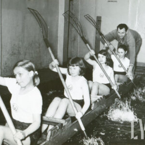 dzieci ubrane w stroje sportowe, trenujący w prowizorycznym kajaku i przy pomocy prowizorycznych wioseł