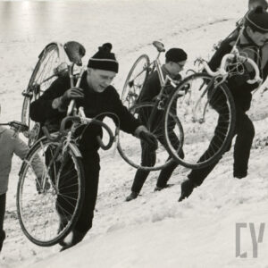 mężczyźni w dresach z czapkami na głowach wdrapujący się pod górę z rowerami na ramieniu