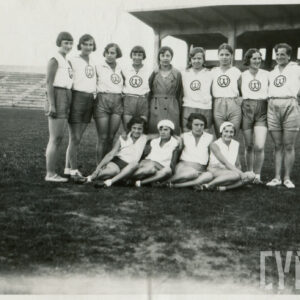 grupa kobiet w strojach sportowych, pozująca do fotografii na tle drewnianych trybun stadionu