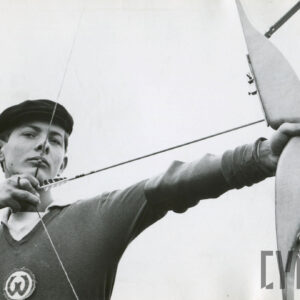 młody mężczyzna w stroju sportowym z herbem klubowym na piersi, mierzący do celu z łuku