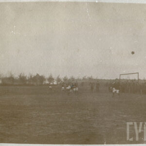 grupa osób grających w piłkę na prowizorycznym boisku, przy którym stoi grupa widzów