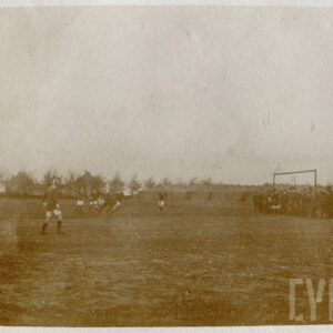 grupa osób grających w piłkę na prowizorycznym boisku, przy którym stoi grupa widzów