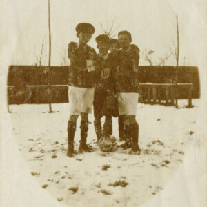 czterech chłopców ubranych w stroje sportowe, stojących z piłką na boisku pokrytym śniegiem 