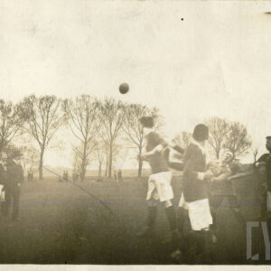 grupa młodych ludzi grająca w piłkę w strojach sportowych na prowizorycznym boisku otoczonym drzewami