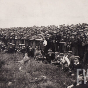 tłum ludzi stojących i leżących na trawie, obserwujący zawody sportowe