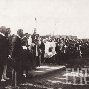 dwóch duchownych oraz duża grupa odświętnie ubranych ludzi stojąca na boisku sportowym