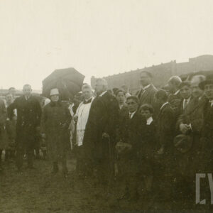 przemawiający starszy mężczyzna otoczony tłumem osób, wszyscy elegancko ubrani, stoją na boisku piłkarskim 