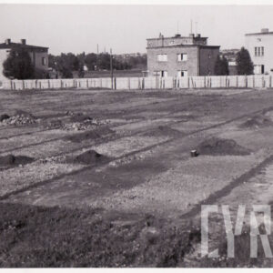 duży pusty teren trawiasto-ziemny, otoczony parkanem, w głębi ceglane budynki mieszkalne